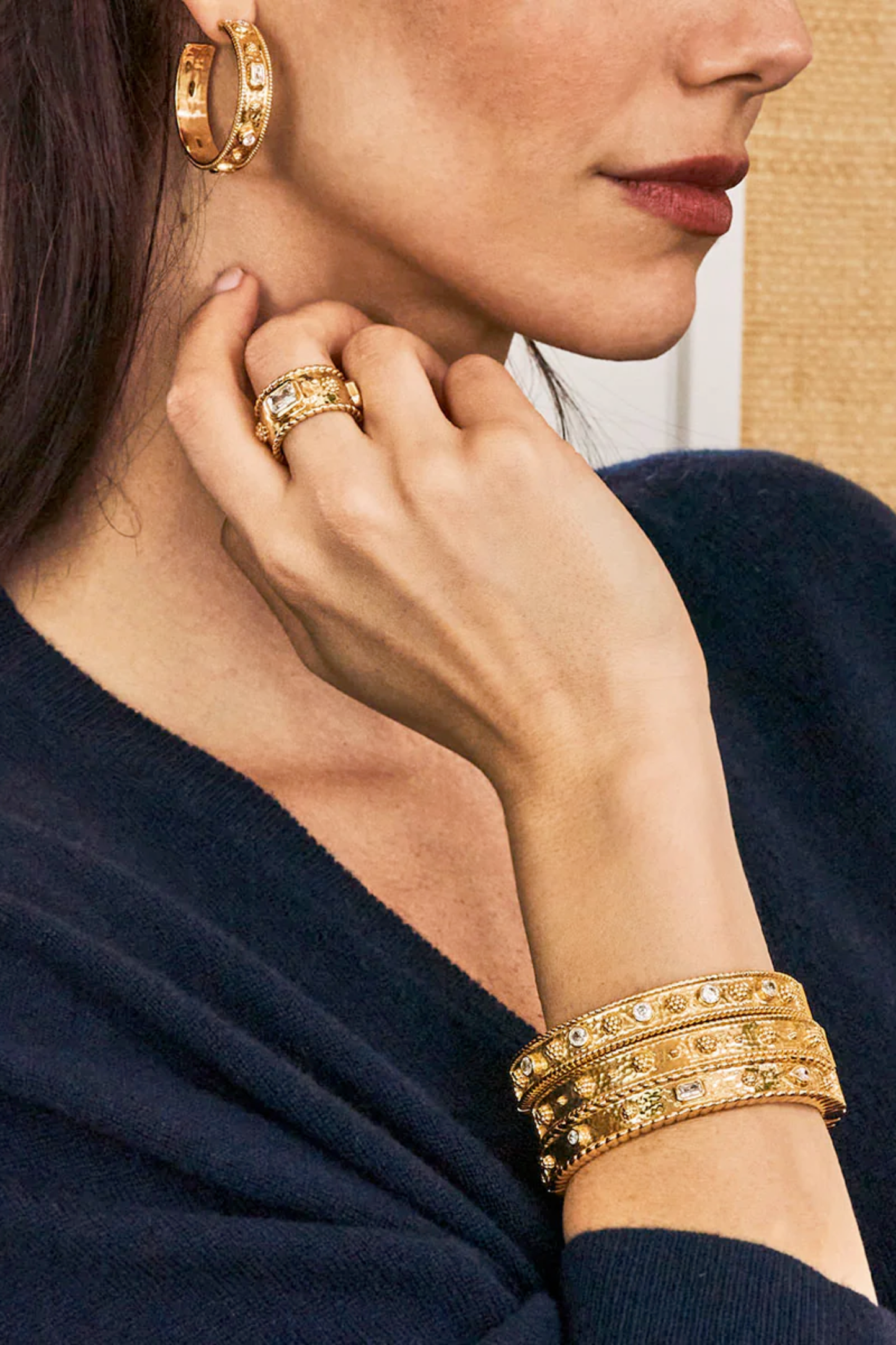 Close-up of a woman wearing gold jewelry including earrings, ring, and bracelets.