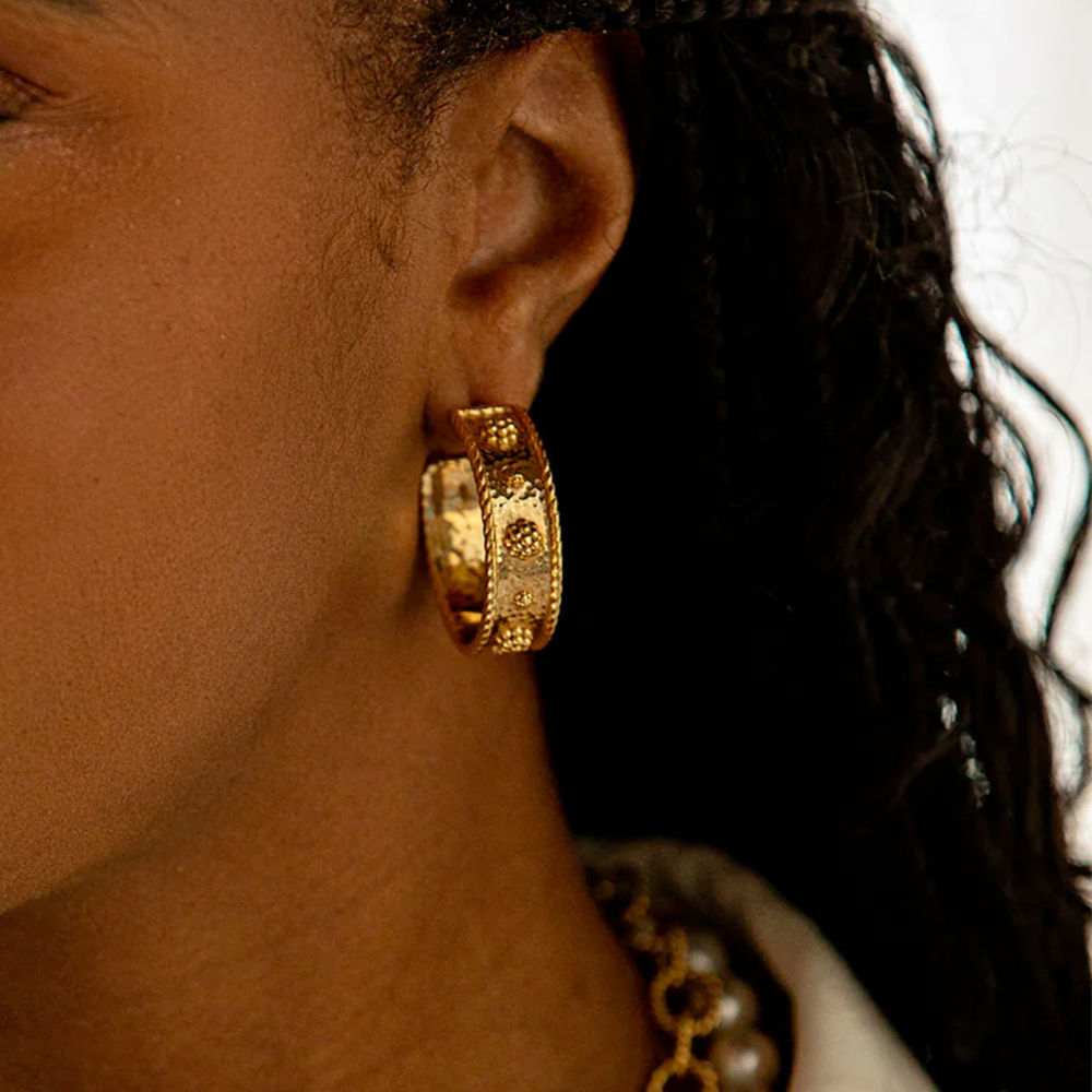 Close-up of a person wearing gold hoop earrings with a blurred background
