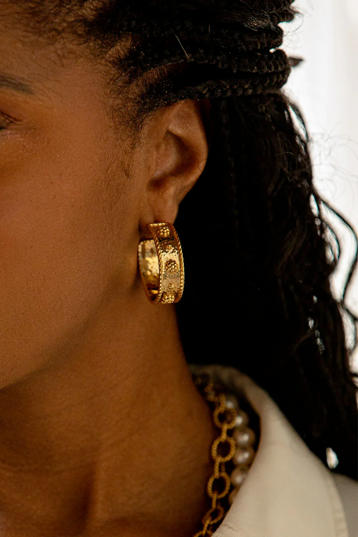 Close-up of a person wearing gold hoop earrings with a blurred background
