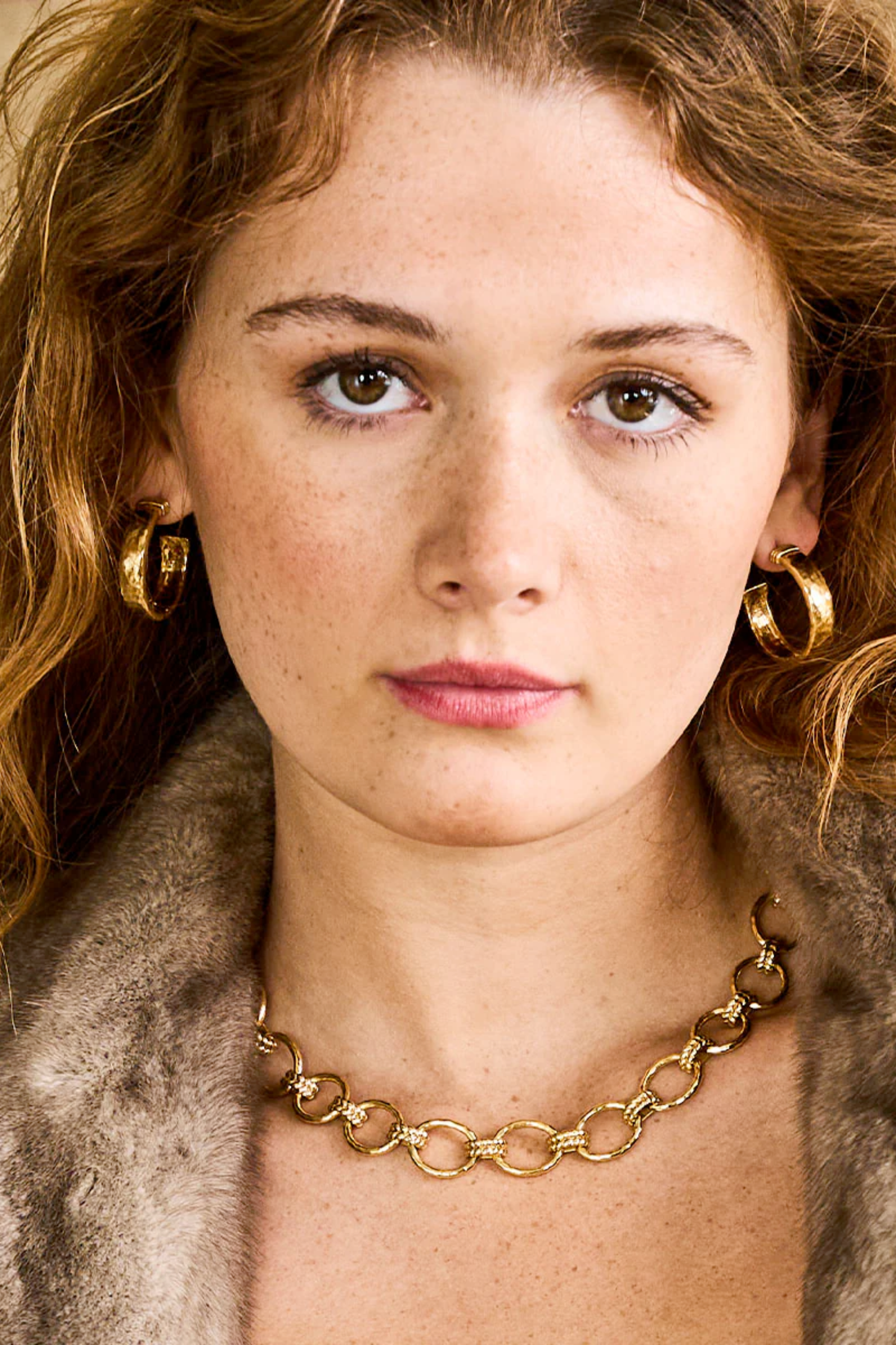 Close-up of a woman wearing gold earrings and a gold necklace, with a fur coat.