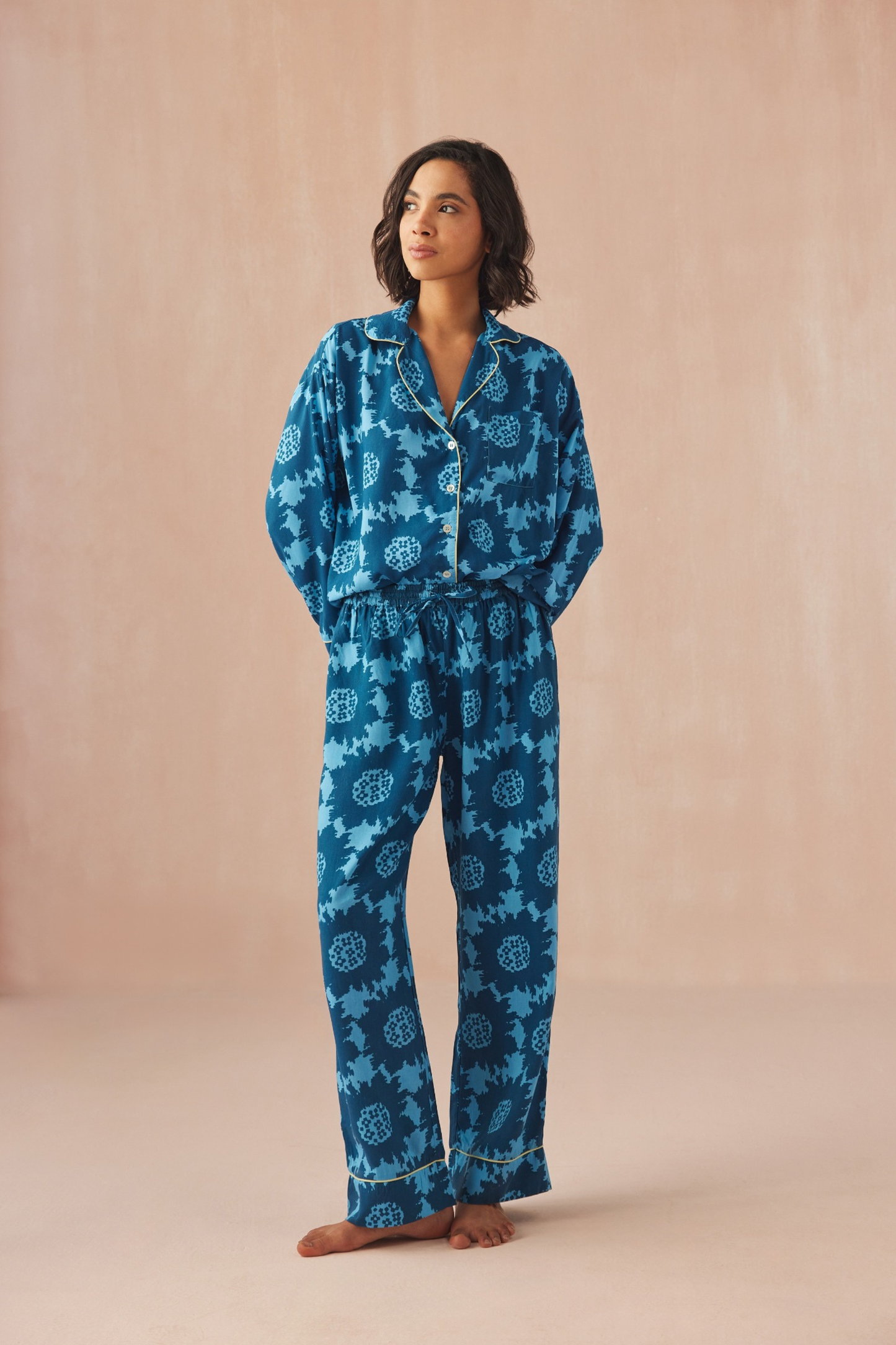 Woman wearing patterned pajamas from Omika standing against a beige background